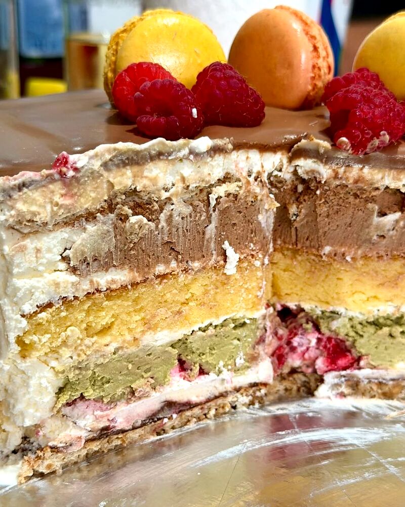 Felie de tort cu straturi de cremă, fructe de pădure și macarons deasupra