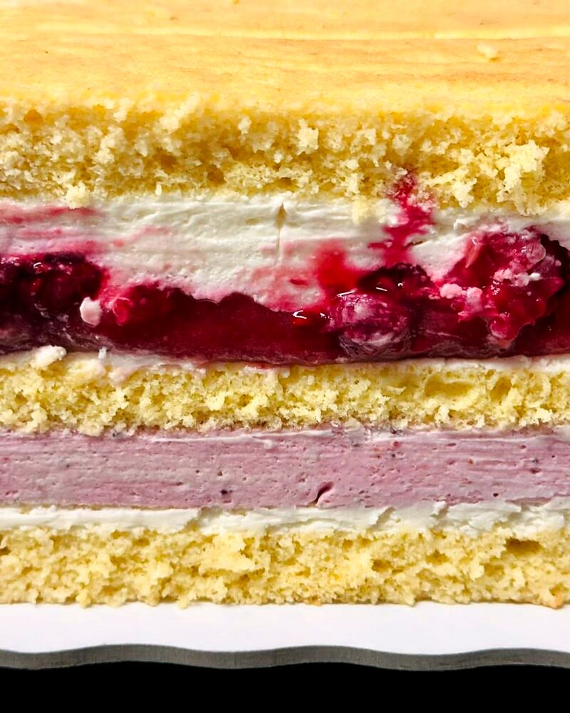 Felie de tort cu strat gros de zmeură între blaturi deschise la culoare