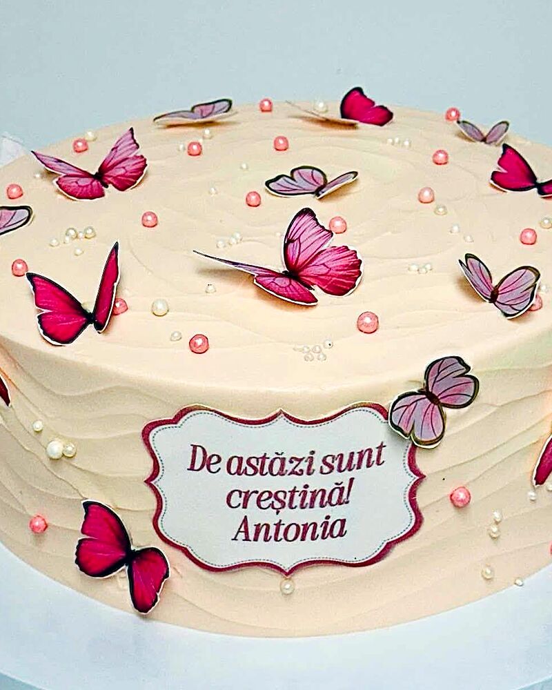 Tort crem cu fluturi roz și medalion cu text scris de mână