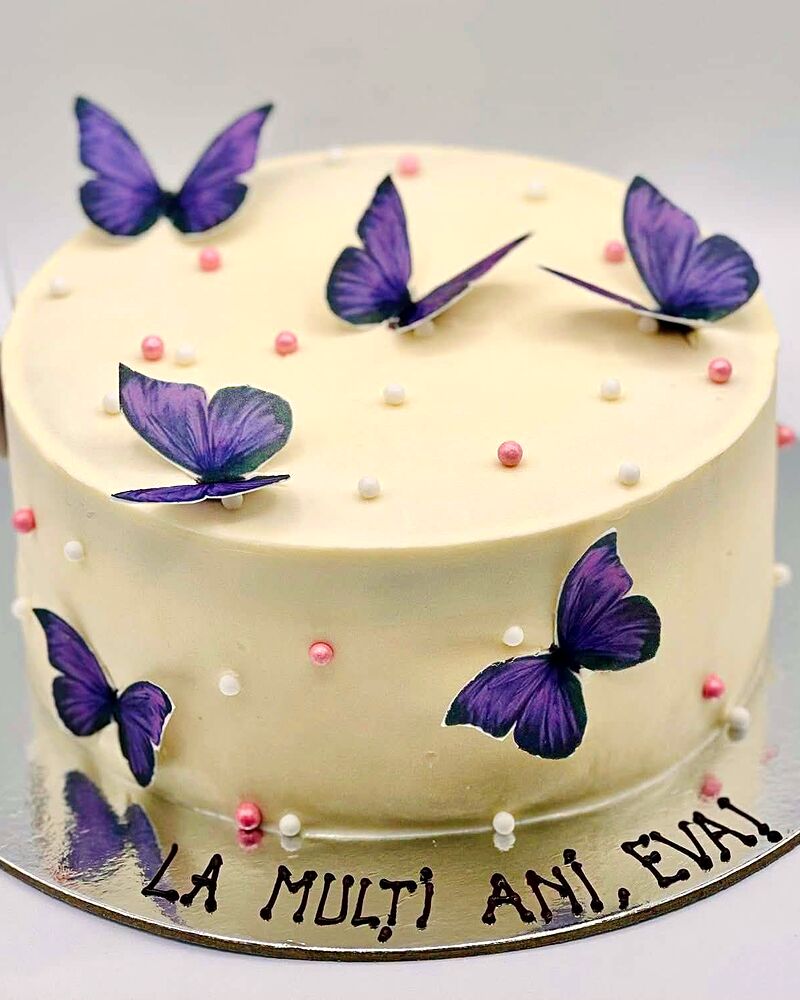 Tort alb decorat cu fluturi mov și bile de zahăr roz